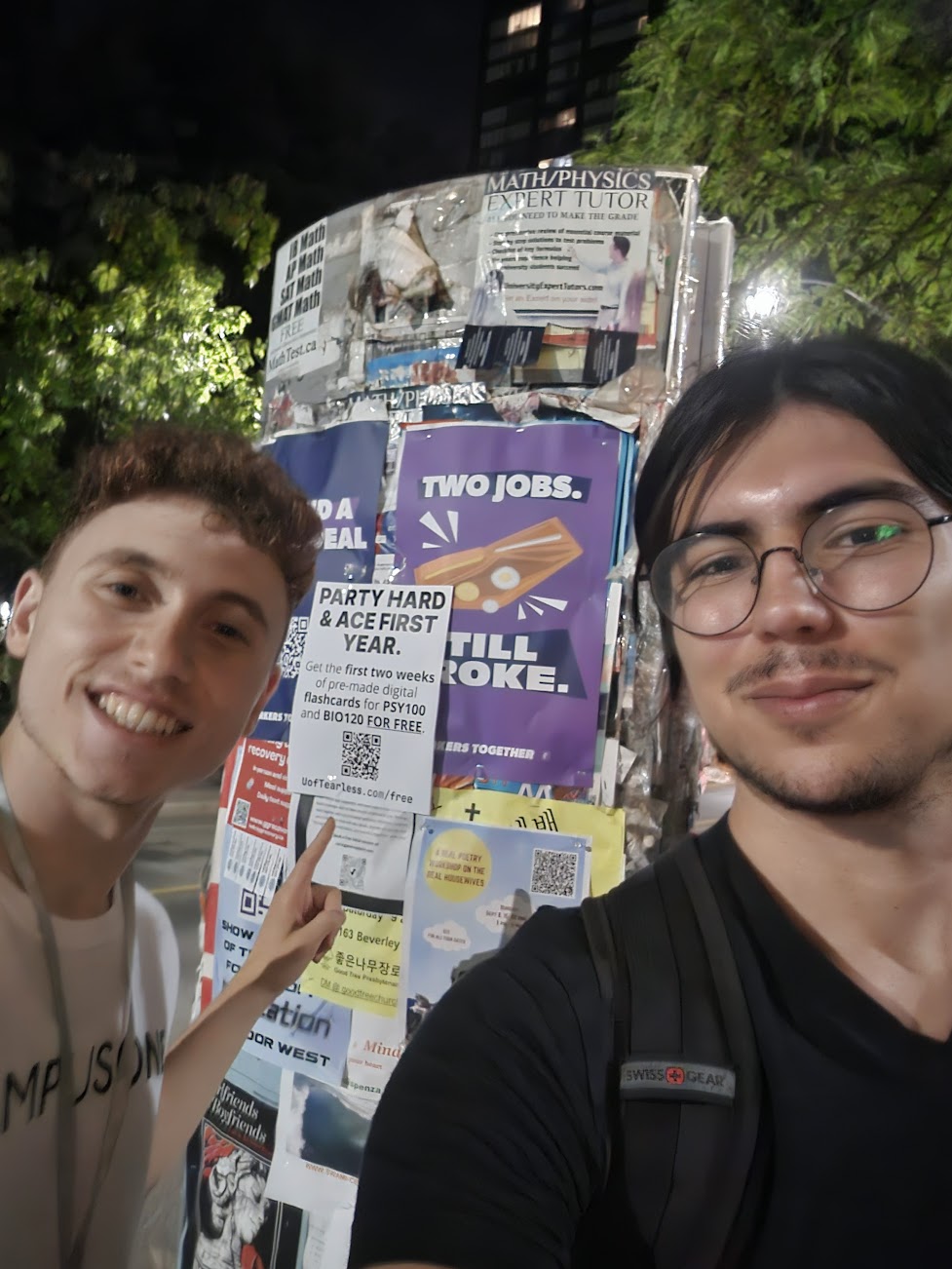 Me and another friend hanging up poster advertisements for UofTearless. The poster reads: 'PARTY HARD & ACE FIRST YEAR. Get the first two weeks of pre-made digital flashcards for PSY100 and BIO120 FOR FREE. uoftearless.com/free'